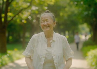 Older Asian woman smiling as she walks along a tree-lined park path