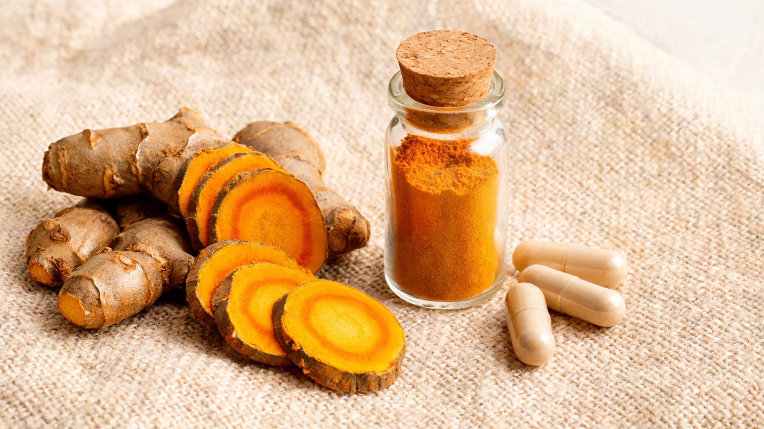 Fresh turmeric rhizomes and curcumin powder on a warm linen surface