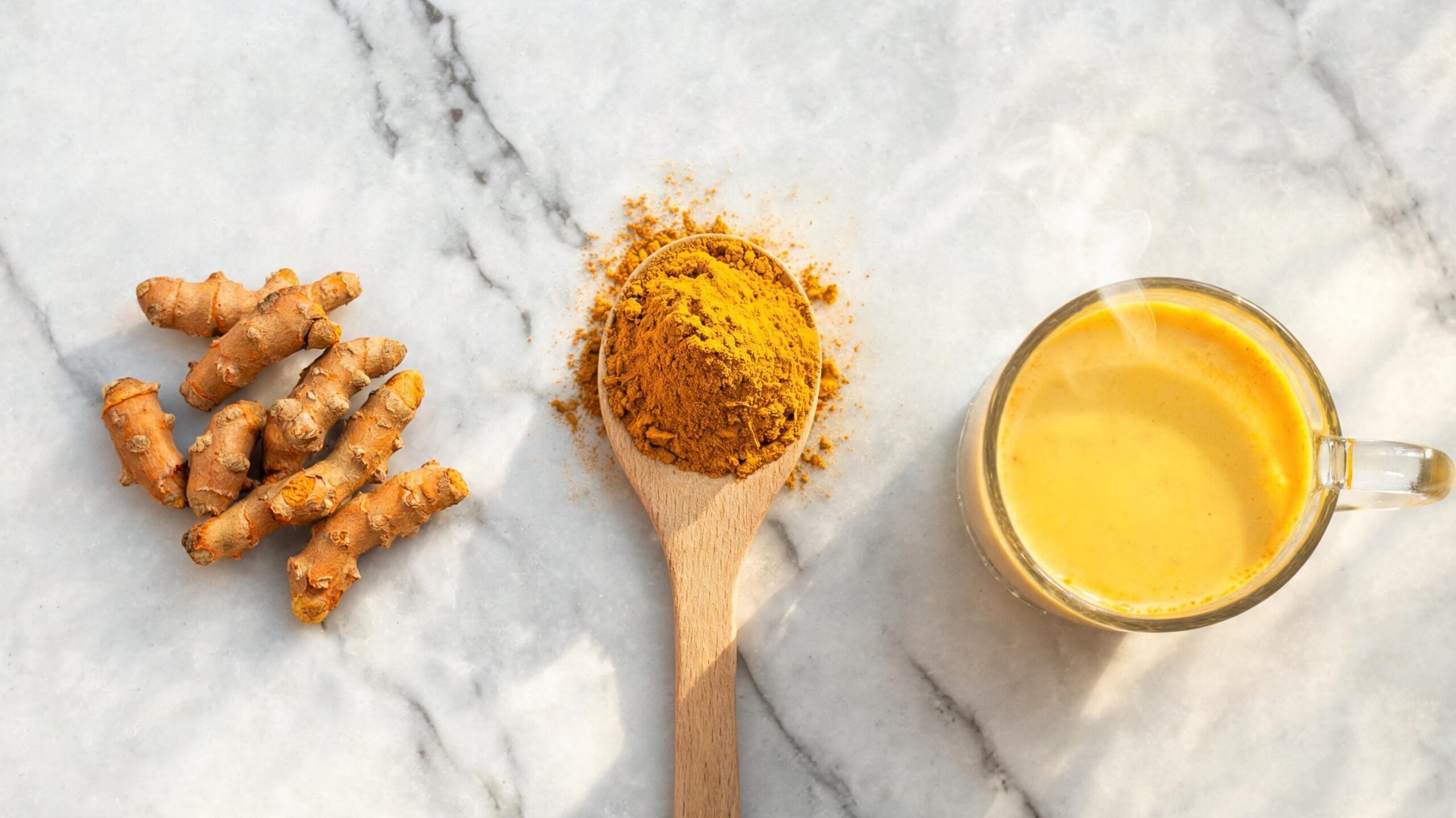 Wooden spoon with golden curcumin powder and dried turmeric roots on marble
