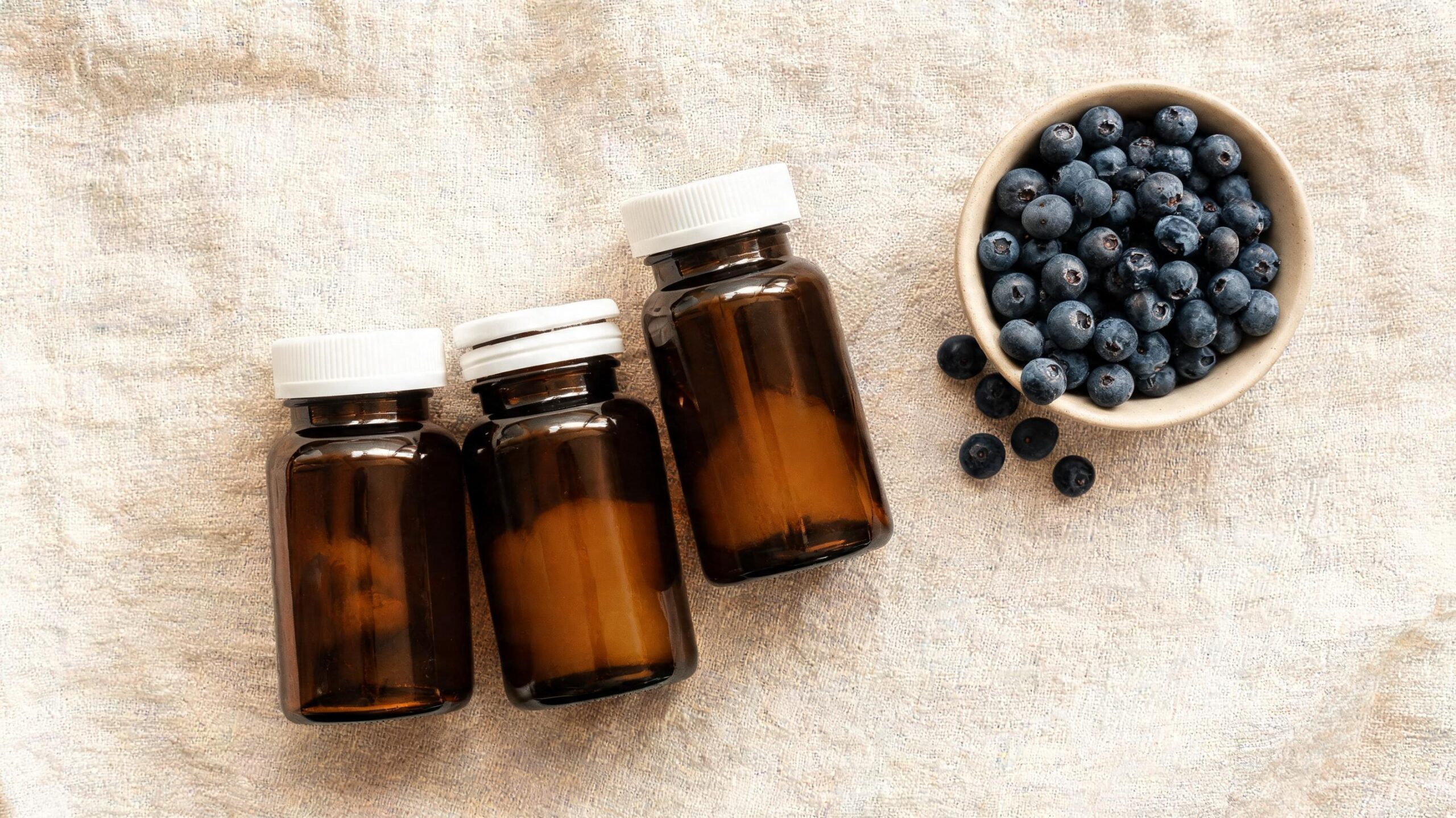 Amber glass supplement bottles with fresh bilberries on linen surface