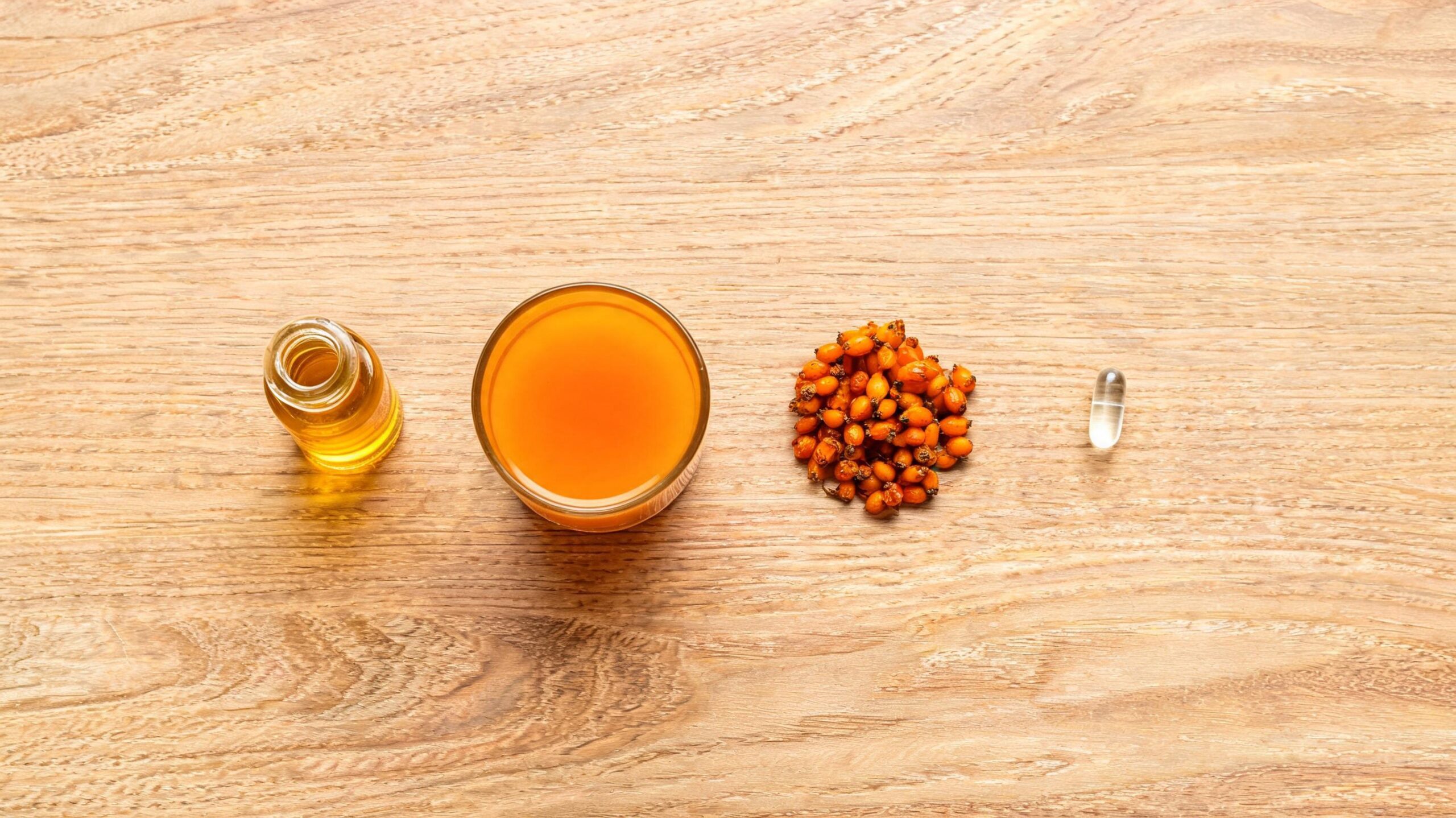 Small amber dropper bottle of golden sea buckthorn oil beside a ceramic dish of fresh orange sea buckthorn berries on a rustic wooden table in warm morning light